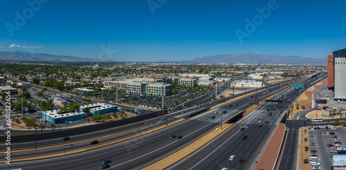 Aerial view of a bustling Las Vegas cityscape with a busy highway  surrounded by modern beige buildings  green spaces  and mountains under a clear blue sky.