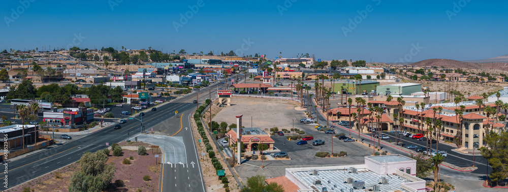 Aerial view of a Barstow U.S. town nestled in a desert valley, featuring beige and brown buildings with terracotta roofs, palm trees, and a grid-like street layout.