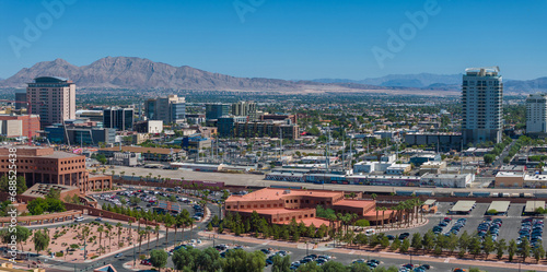Aerial cityscape with modern high-rises, surrounded by mountains under a clear blue sky, featuring a busy parking lot in Las Vegas, USA.