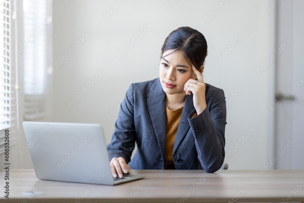 Portrait of young Business asian woman using computer at home sitting in the office working and studying alone. Thoughtful serious woman thinking on new projects. Portrait of young Business asian woman using computer at home sitting in the office working and studying alone. Thoughtful serious woman thinking on new projects.