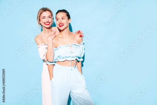 Two young beautiful smiling brunette hipster female in trendy summer clothes. Sexy carefree women posing near blue wall in studio. Positive models having fun. Cheerful and happy