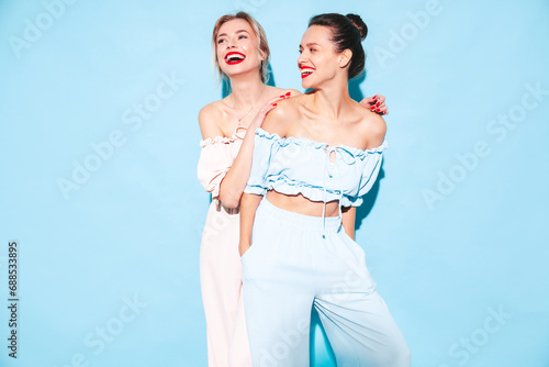 Two young beautiful smiling brunette hipster female in trendy summer clothes. Sexy carefree women posing near blue wall in studio. Positive models having fun. Cheerful and happy