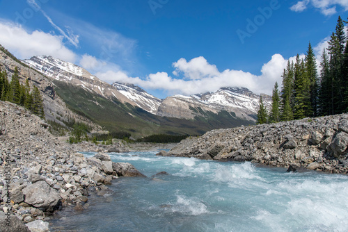 Low angle view over the swirling water of the river near The Big Bend, Alberta, Canada, towards the snowcapped Cirrus Mountain range in the background against a white clouded blue sky