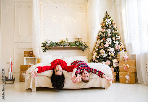 smiling happy mother and son wearing red pajamas posing and having fun on the bed near christmas tree in decorated bedroom