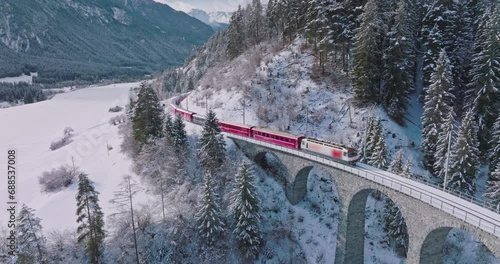 Landwasser Viaduct world heritage sight with luxury Glacier and Bernina express in Swiss Alps snow winter scenery. Aerial Drone shot red train passing through famous mountain in Filisur, Switzerland.