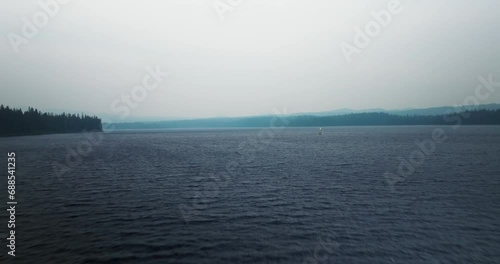 Aerial dolly over foggy cold lake to sunfish sailboat on windswept water