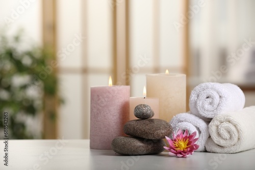 Spa composition. Burning candles, lotus flower, stones and towels on white table indoors, space for text
