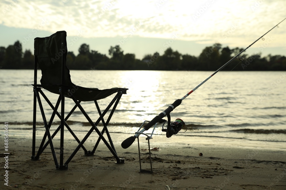 Folding chair and fishing rod on sand near river Folding chair and fishing rod on sand near river