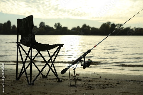 Folding chair and fishing rod on sand near river