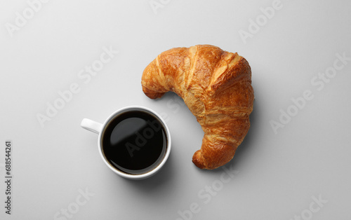 Delicious fresh croissant and cup of coffee on light background, flat lay