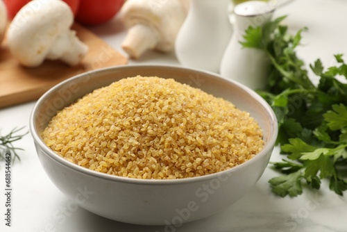 Raw bulgur in bowl and spices on white table, closeup