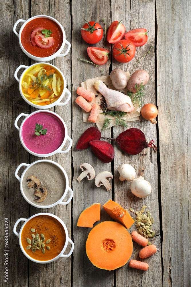 Tasty broth, different cream soups in bowls and ingredients on old wooden table, flat lay