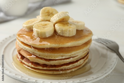Delicious pancakes with bananas and honey on white table, closeup