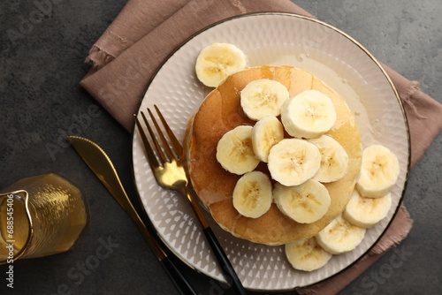 Tasty pancakes with sliced banana and honey served on gray table, flat lay