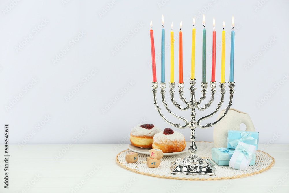 Hanukkah celebration. Menorah with burning candles, dreidels, donuts and gift boxes on white wooden table, space for text Hanukkah celebration. Menorah with burning candles, dreidels, donuts and gift boxes on white wooden table, space for text