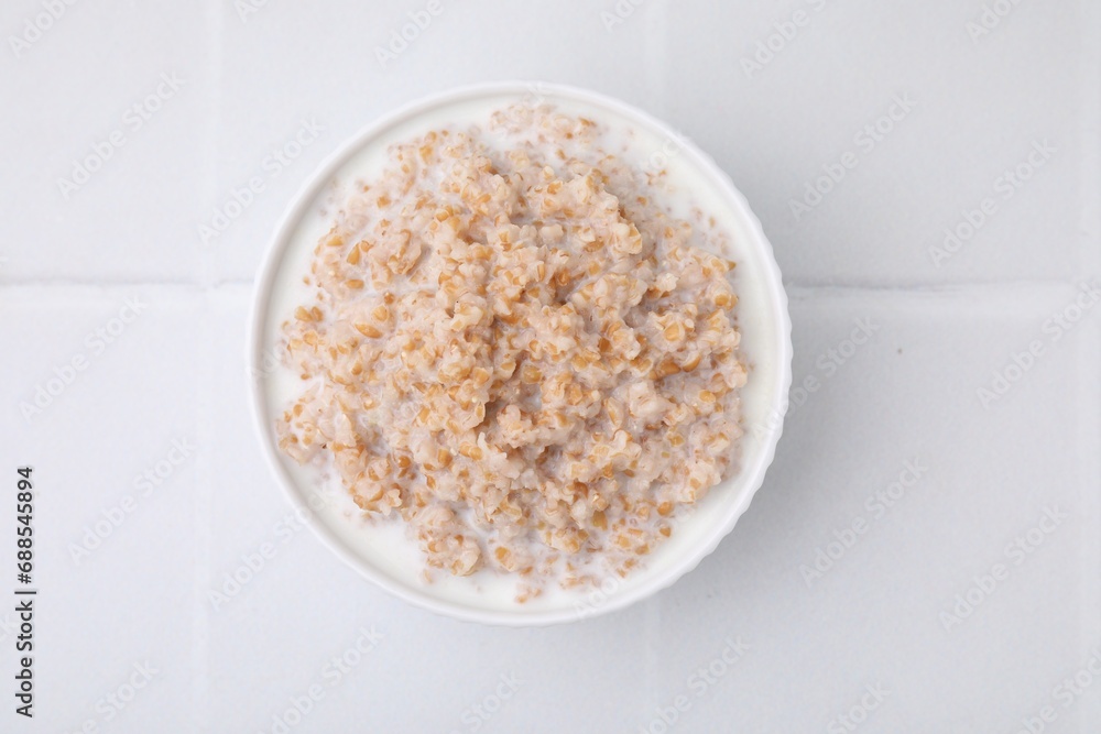 Tasty wheat porridge with milk in bowl on white table, top view Tasty wheat porridge with milk in bowl on white table, top view