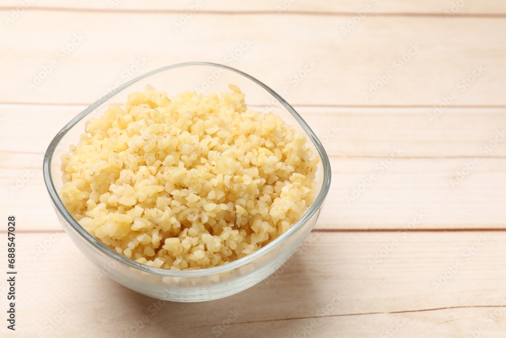 Delicious bulgur in glass bowl on wooden table, closeup. Space for text Delicious bulgur in glass bowl on wooden table, closeup. Space for text