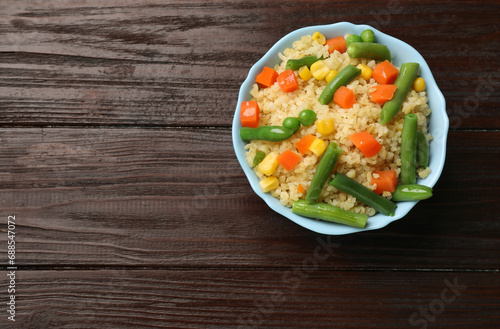 Delicious bulgur with vegetables in bowl on wooden table, top view. Space for text