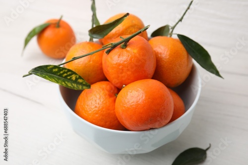 Bowl with fresh ripe tangerines and leaves on white table