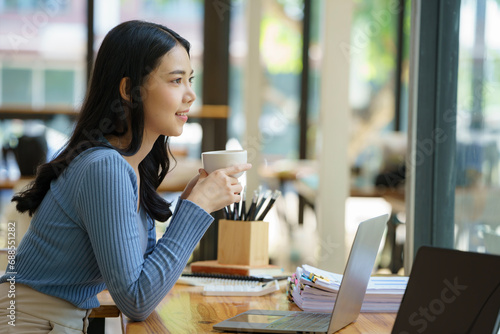 Beautiful young asian business woman drinking coffee and using laptop computer while working in office.