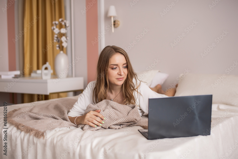 Cute girl is working on a laptop while lying at home on a bed Cute girl is working on a laptop while lying at home on a bed