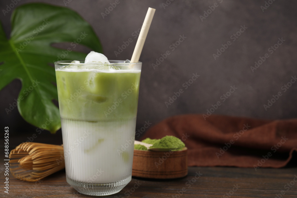 Glass of tasty iced matcha latte, bamboo whisk and powder on wooden table. Space for text Glass of tasty iced matcha latte, bamboo whisk and powder on wooden table. Space for text
