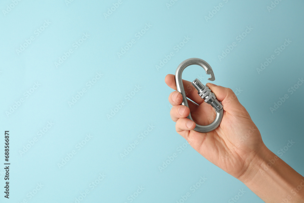 Man with metal carabiner on light blue background, closeup. Space for text