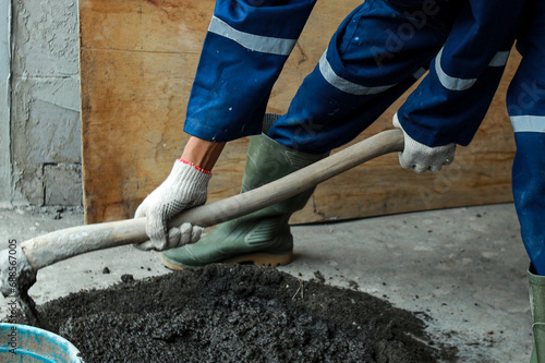 Male worker with safety rubber boot and uniform using hoe to mixing sand, cement and water for home renovation