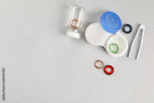 Different color contact lenses, tweezers and containers on light background, flat lay. Space for text