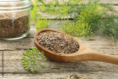 Spoon with dry seeds and fresh dill on wooden table, closeup