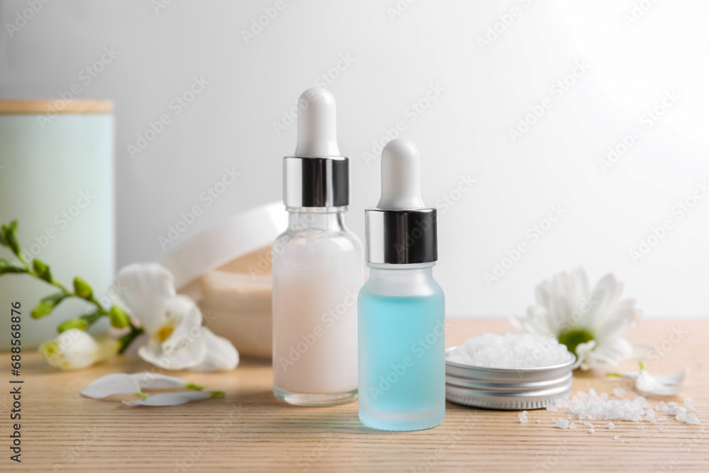 Bottles of cosmetic serum, sea salt and beautiful flowers on wooden table, closeup