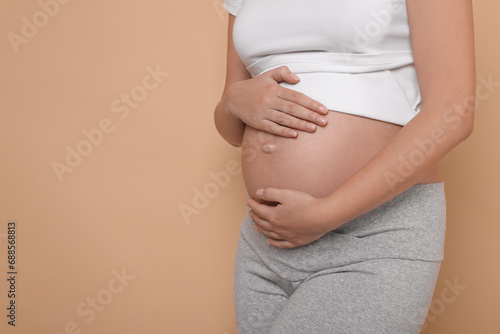 Pregnant woman in white T-shirt on beige background, closeup. Space for text