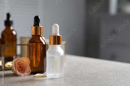 Bottles of cosmetic serum and flower on gray table, closeup. Space for text