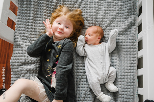 Young girl tenderly hugs her newborn while lying on bed at home. Children hugging together. First meeting baby and toddler older sister. Sibling relationship in family when youngest was born. Top view