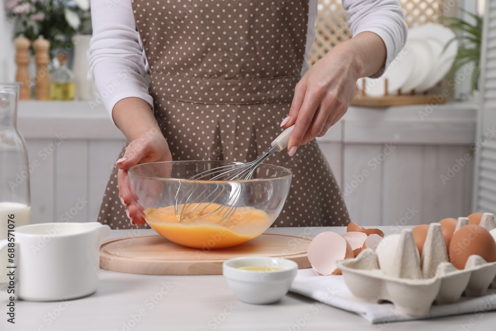 Woman whisking eggs in bowl at table indoors, closeup