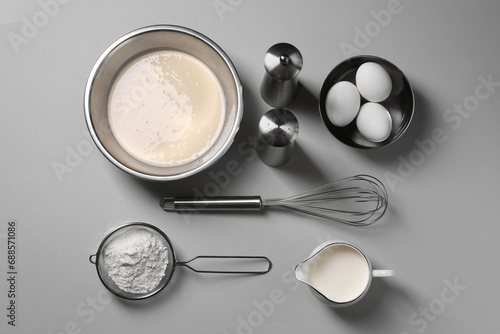Flat lay composition with dough in bowl and metal whisk on grey background photo