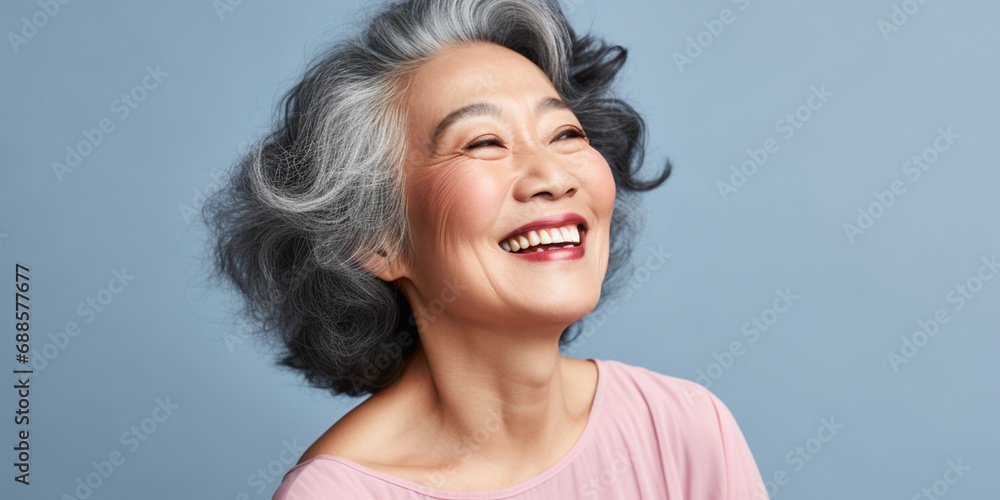 Happy Asian Woman. Portrait of Beautiful Older Mid Aged Mature Smiling Woman in Pink Clothes Isolated on Grey Background. Anti-aging Skin Care Face Beauty Product. Banner with Copy Space. Happy Asian Woman. Portrait of Beautiful Older Mid Aged Mature Smiling Woman in Pink Clothes Isolated on Grey Background. Anti-aging Skin Care Face Beauty Product. Banner with Copy Space.