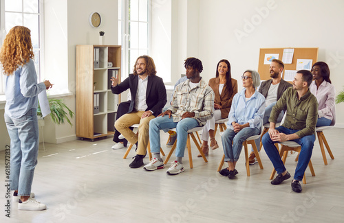 Young woman speaker having business training on a work meeting in the office in front of a group of multiracial diverse people company employees or a team of staff sitting on chairs.