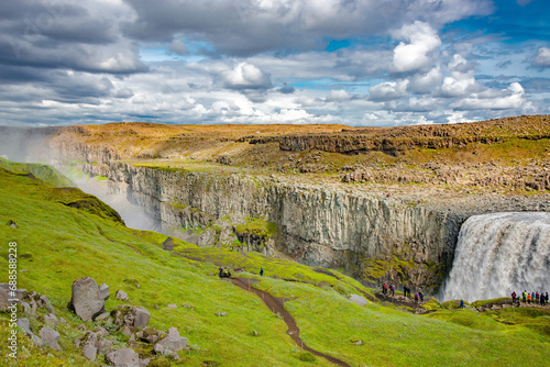 Dettifoss  Iceland. Group of  hikers and tourists at the biggest waterfall in Iceland Dettifoss. Birdview of beautiful Icelandic landscape  huge canyon  rainbow and dramatic sky