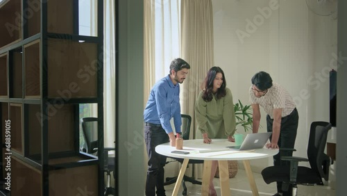 Modern Young Indian Male Female Corporate Executives or Coworkers discussing work together with the help of chart and Laptop in Business startup office. photo
