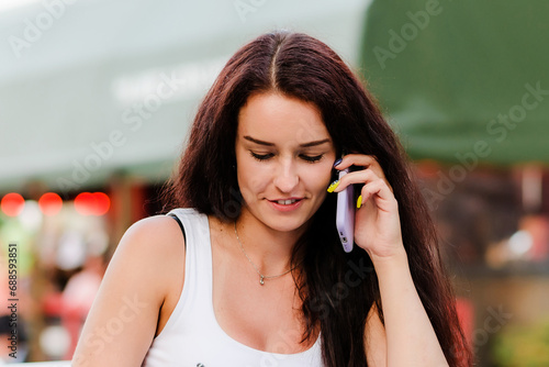 Startup concept.Young smiling beautiful brunette girl sits in summer cafe and calling by phone.Closeup.