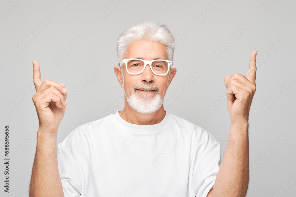 Gray-haired mature man 60 years old in white T-shirt pointing up finger, demonstrating empty space for product or text isolated on white studio background. Gray-haired mature man 60 years old in white T-shirt pointing up finger, demonstrating empty space for product or text isolated on white studio background.