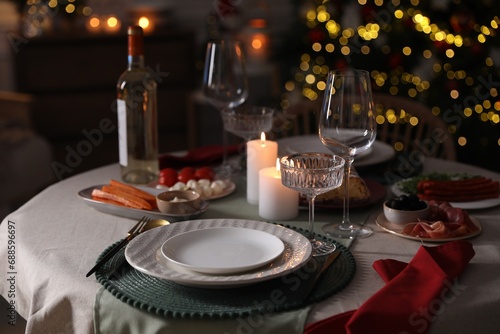 Christmas table setting with burning candles, appetizers and dishware indoors