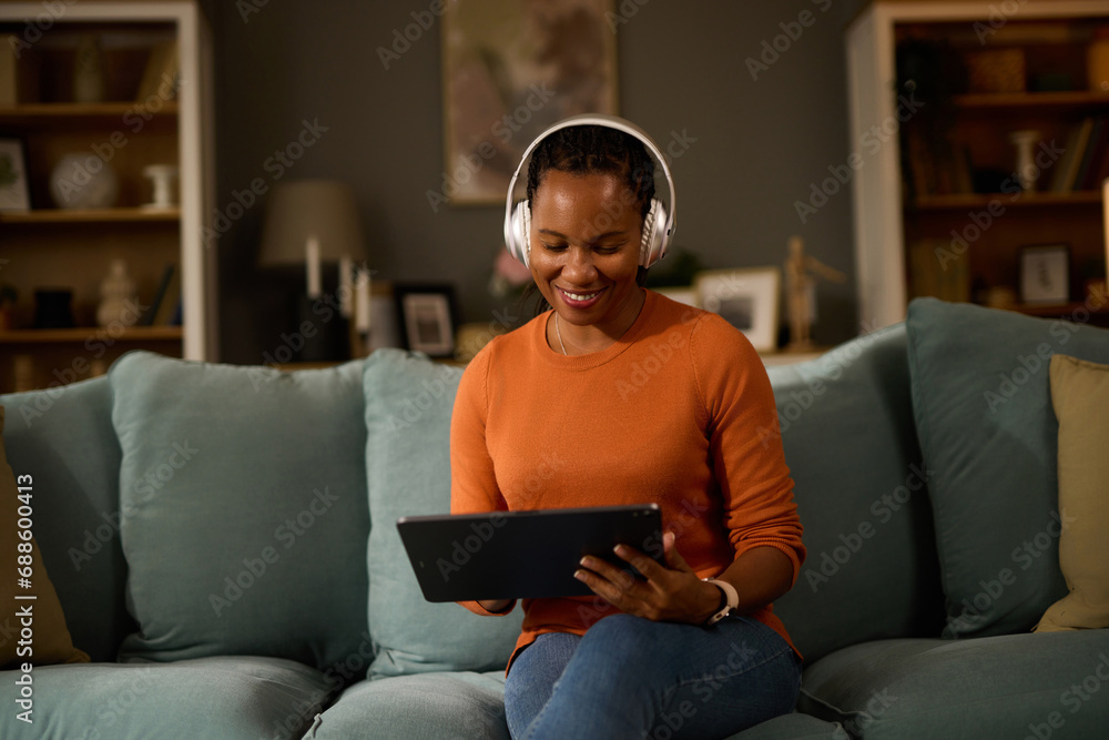 Obraz premium Woman with headphones using tablet computer while relaxing at home