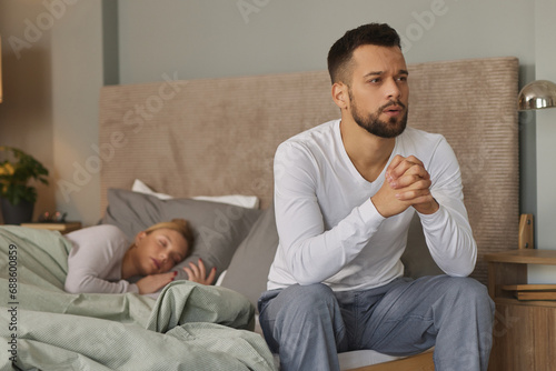 Young man deep in thoughts while his wife sleeps in the background