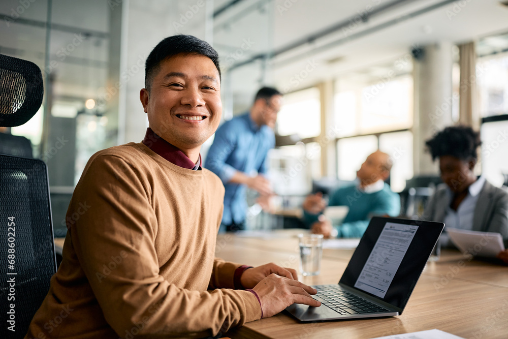 Happy Asian businessman working on laptop during meeting in office and looking at camera. Happy Asian businessman working on laptop during meeting in office and looking at camera.