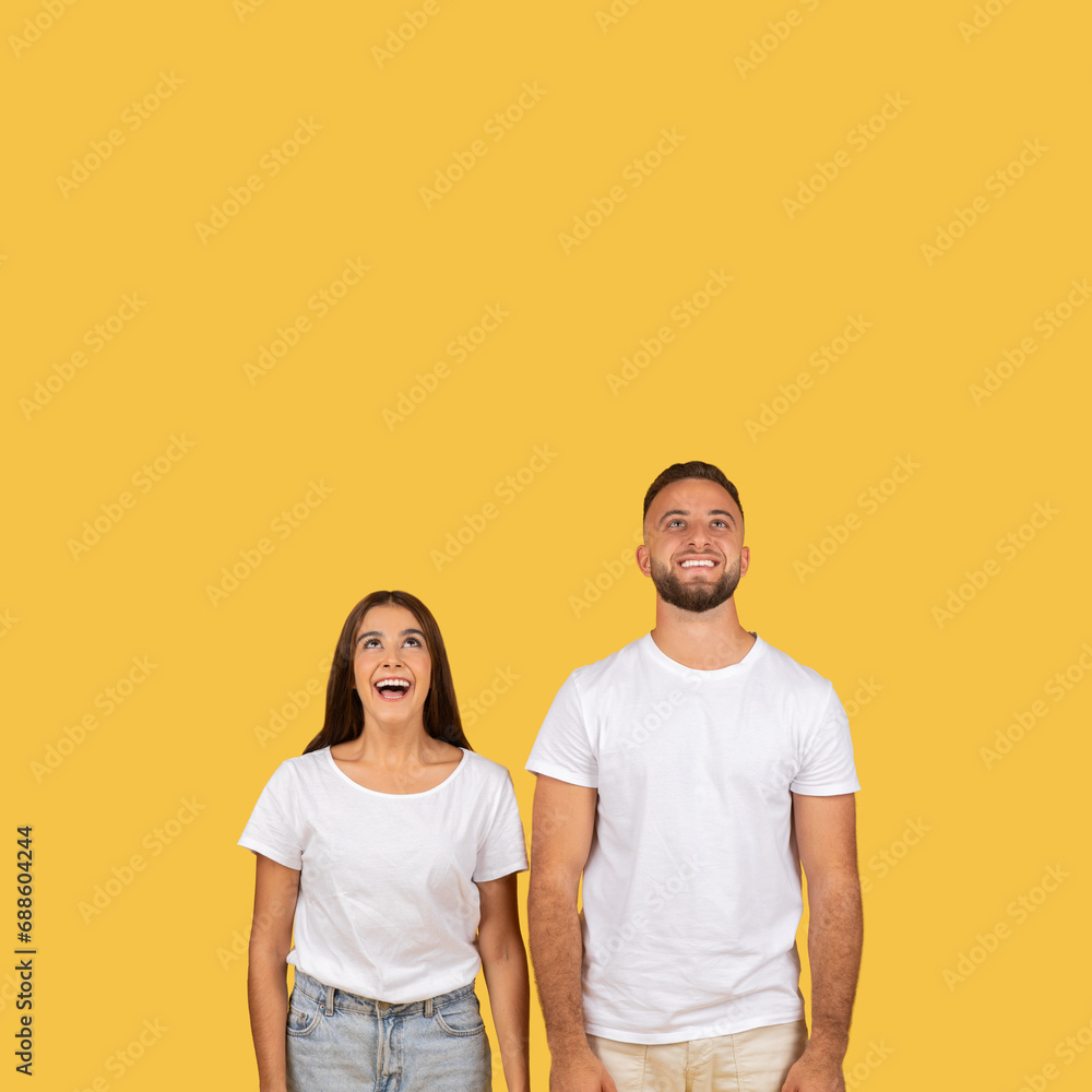 Obraz premium Happy shocked millennial european couple in white t-shirts, look up at empty space
