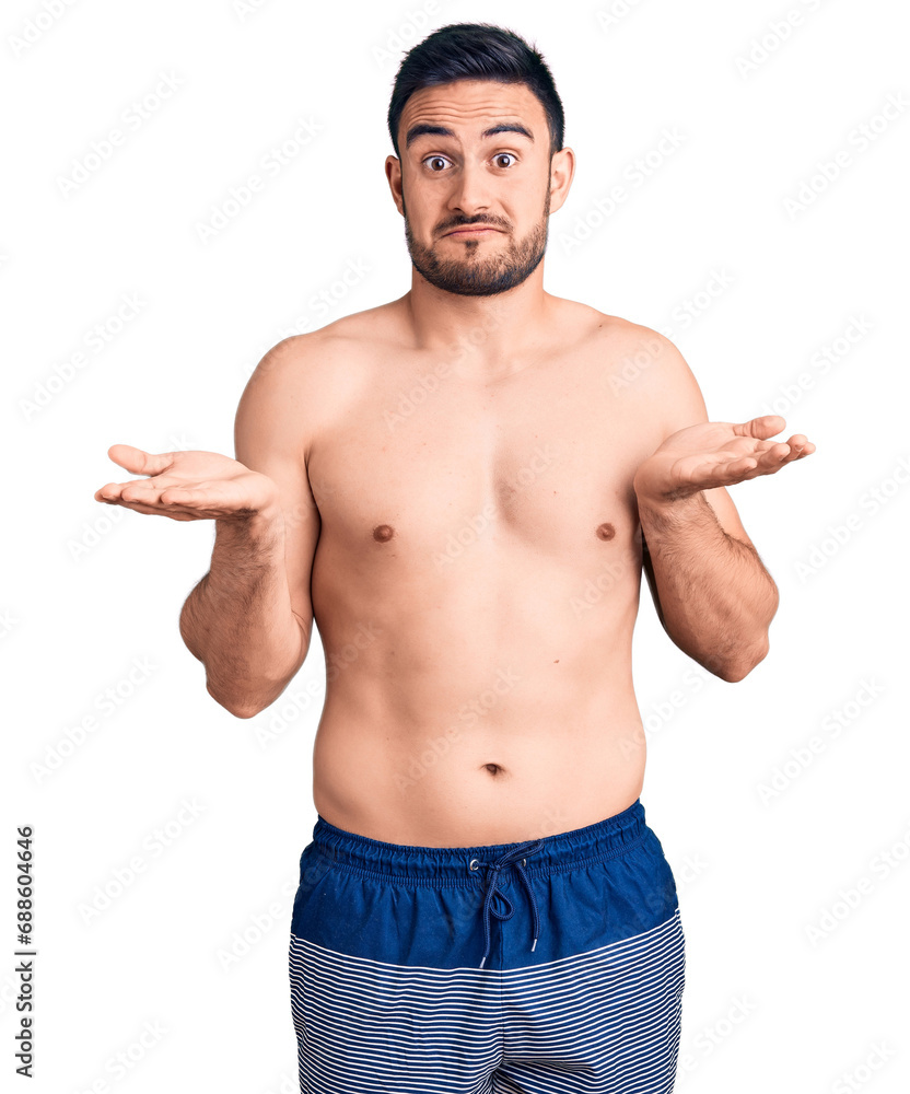 Fototapeta premium Young handsome man wearing swimwear clueless and confused expression with arms and hands raised. doubt concept.