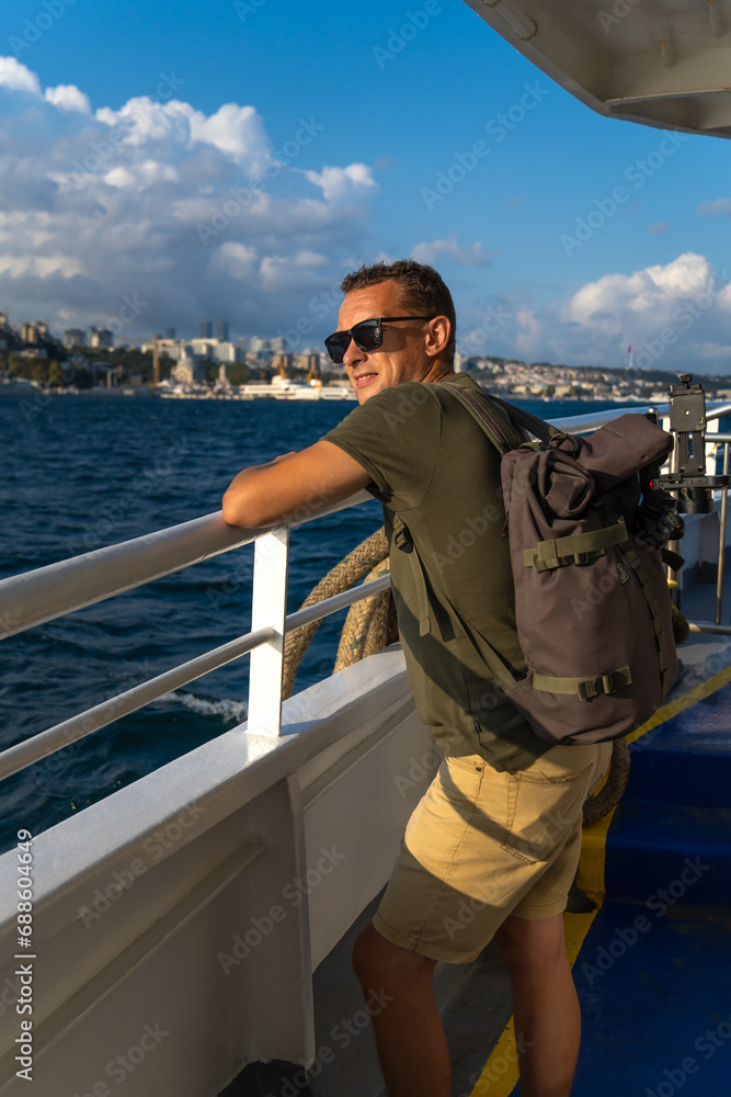 Happy young male tourist with a backpack enjoys the sea and the city from a ferry in Istanbul on a sunny day. Concept of travel, tourism. Vertical photo