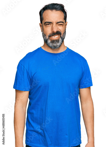 Middle aged man with beard wearing casual blue t shirt winking looking at the camera with sexy expression, cheerful and happy face.